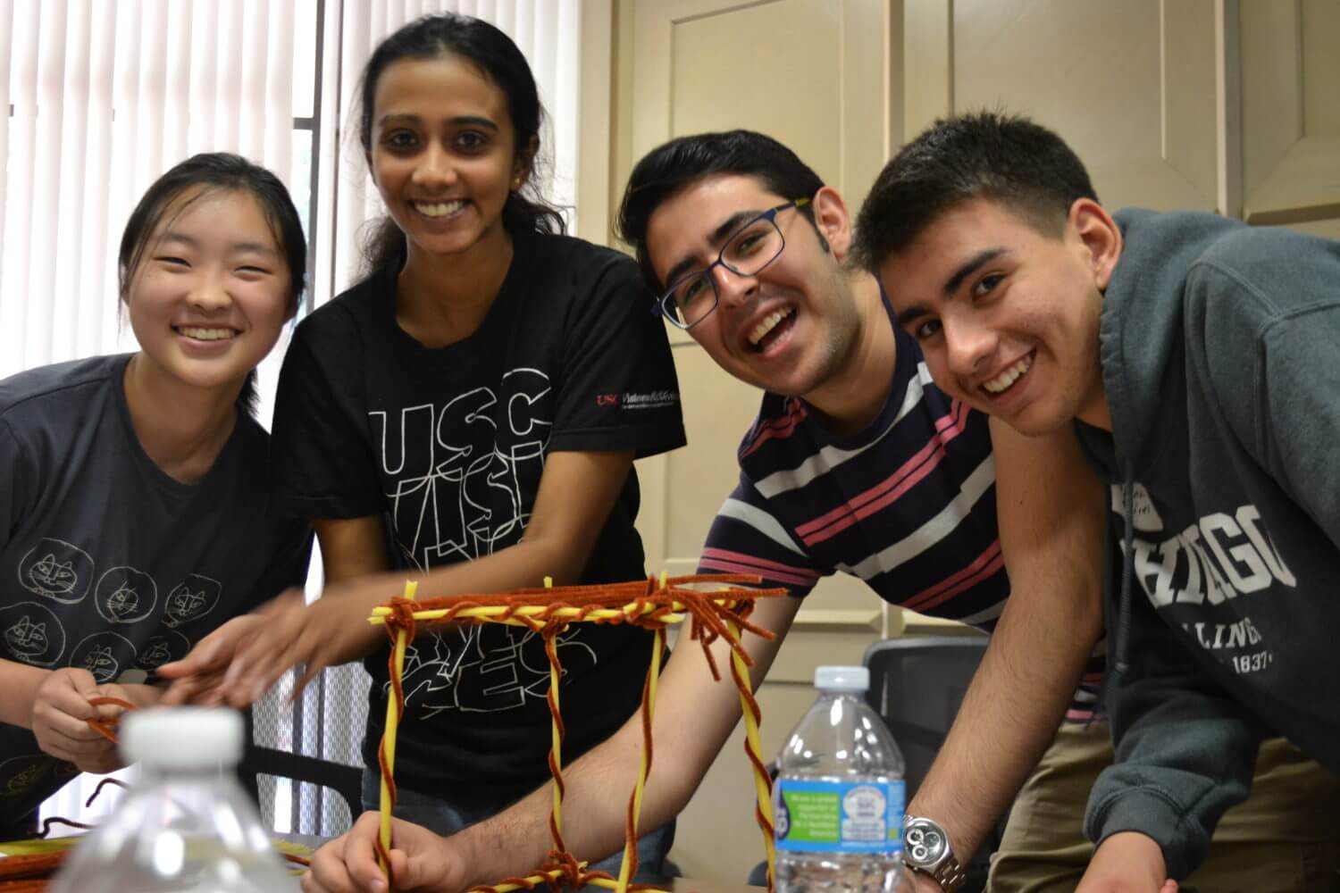 4 student smiling and building a structure with pipe cleaners 