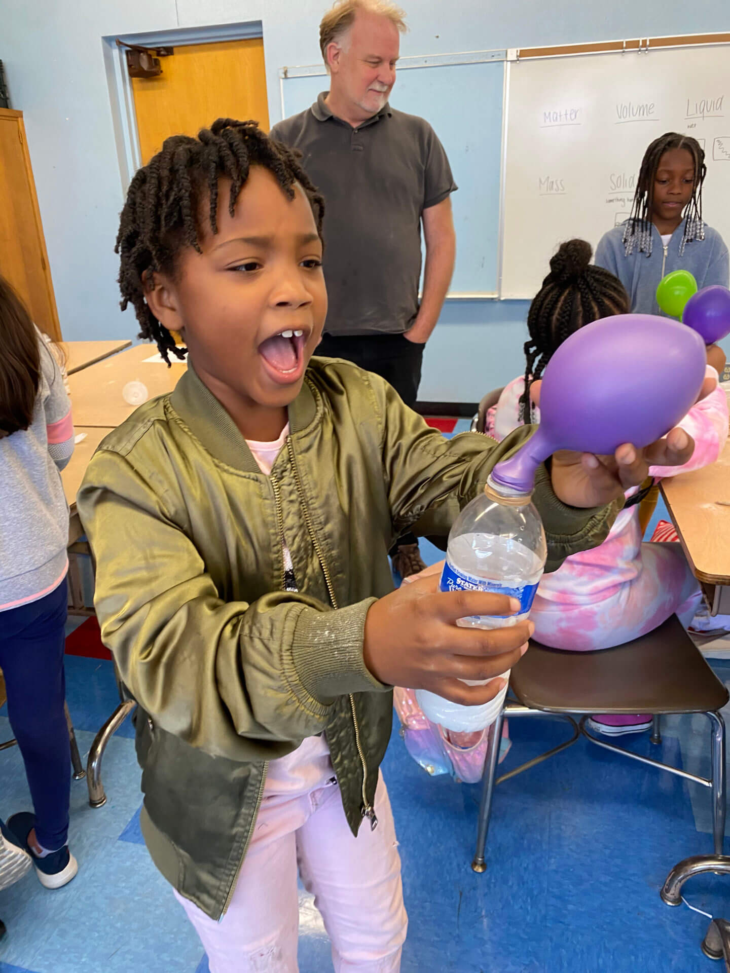 Student looking excited as he is holding a water bottle that a balloon is attached to. 